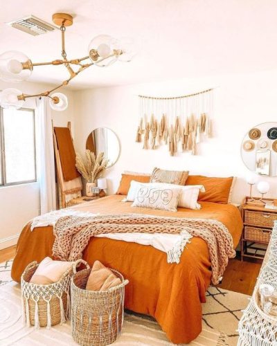 Chambre adulte. Murs blancs, draps orange, panier en osier et meubles bois clair